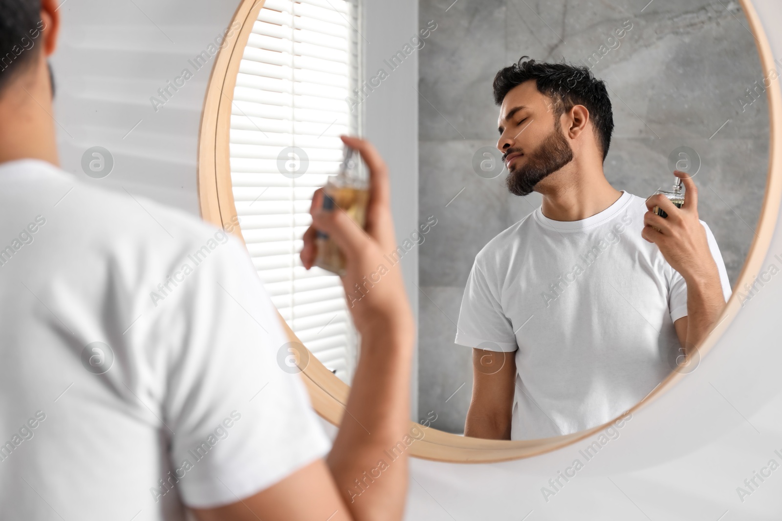 Photo of Man spraying luxury perfume near mirror indoors