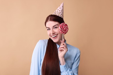 Happy woman in party hat with lollipop on beige background