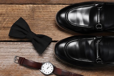 Photo of Stylish black bow tie, wristwatch and shoes on wooden background, flat lay