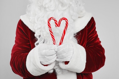 Photo of Santa Claus holding candy canes on light grey background, closeup