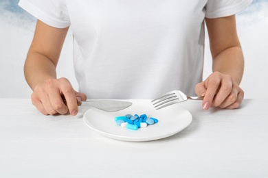 Photo of Woman sitting at table with cutlery and plate of weight loss pills, closeup