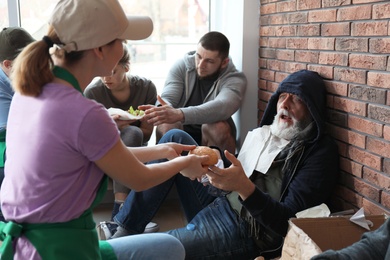 Photo of Volunteer giving food to poor senior man indoors