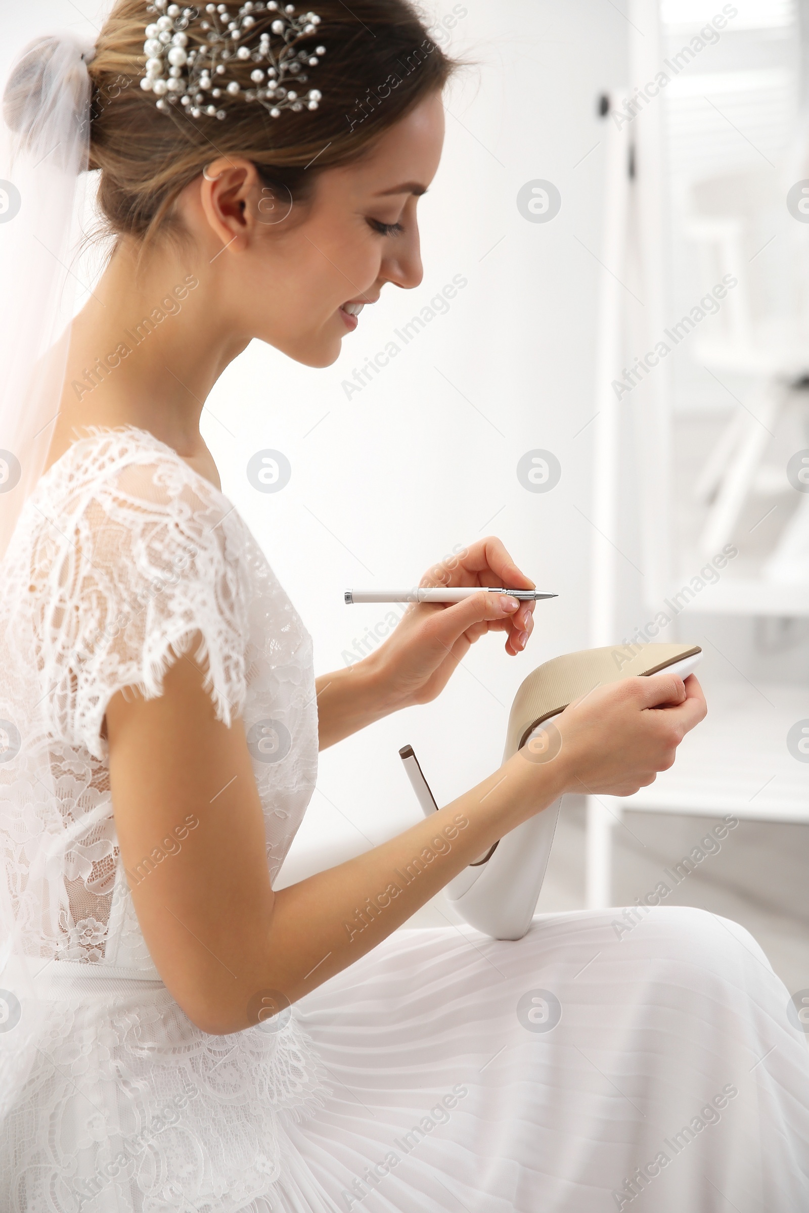 Photo of Young bride writing on her shoe indoors. Wedding superstition