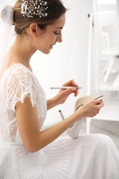 Photo of Young bride writing on her shoe indoors. Wedding superstition