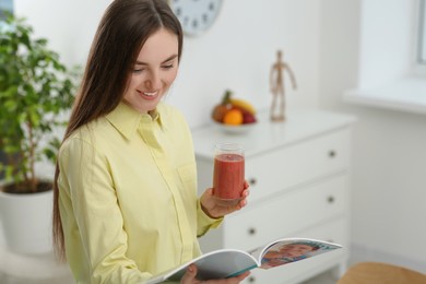 Photo of Beautiful young woman with delicious smoothie reading magazine at home. Space for text