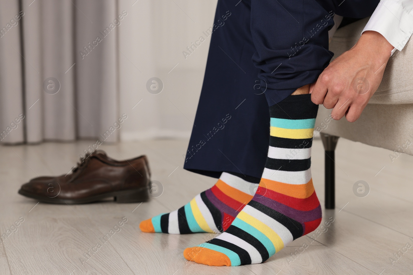 Photo of Man putting on colorful socks indoors, closeup