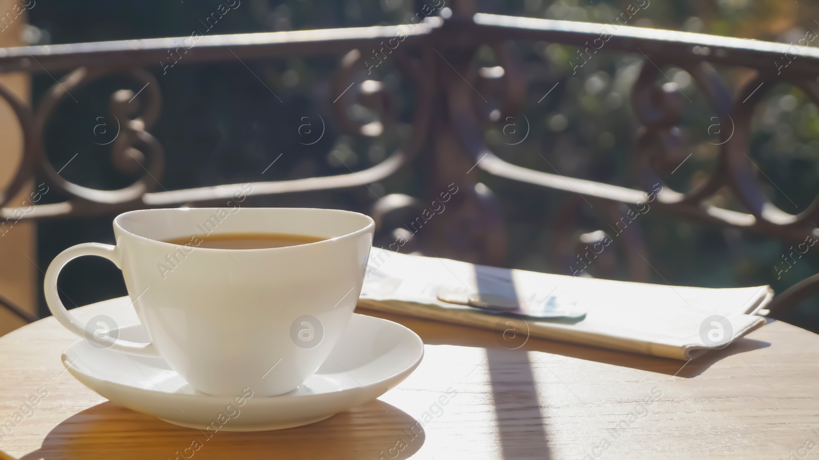 Photo of Cup of aromatic coffee and newspaper on wooden table outdoors, space for text