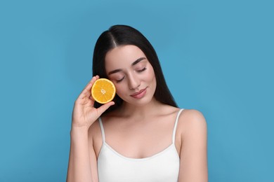 Beautiful young woman with piece of orange on light blue background