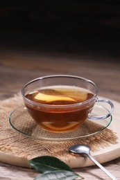 Photo of Aromatic hot tea in glass cup and leaves on wooden table