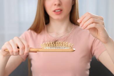 Photo of Woman untangling her lost hair from brush indoors, closeup. Alopecia problem