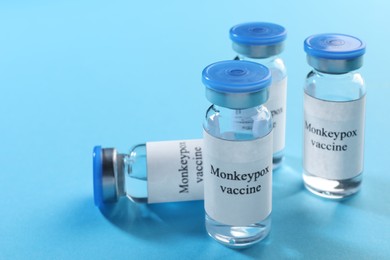 Monkeypox vaccine in glass vials on light blue background, space for text