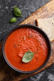 Photo of Delicious tomato cream soup in bowl and basil leaves on dark textured table, flat lay