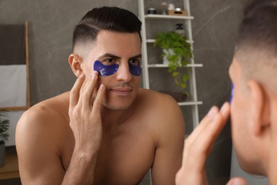 Photo of Man applying blue under eye patches near mirror at home