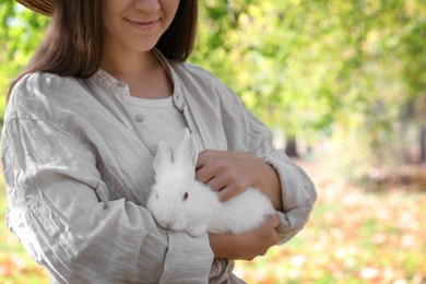 Woman holding cute white rabbit in park, closeup