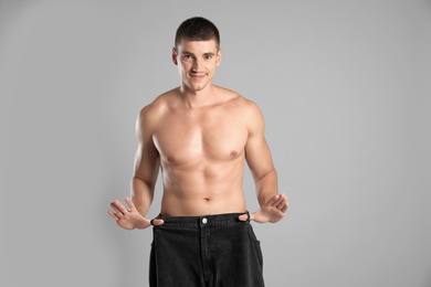 Photo of Young man with slim body in old big size jeans on grey background