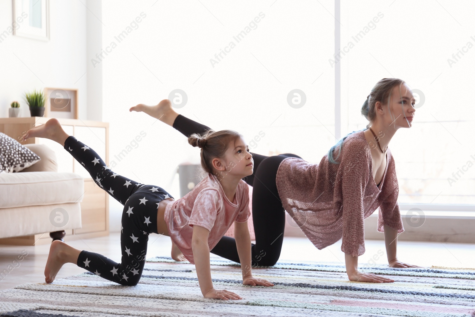 Photo of Young mother and her daughter practicing yoga at home