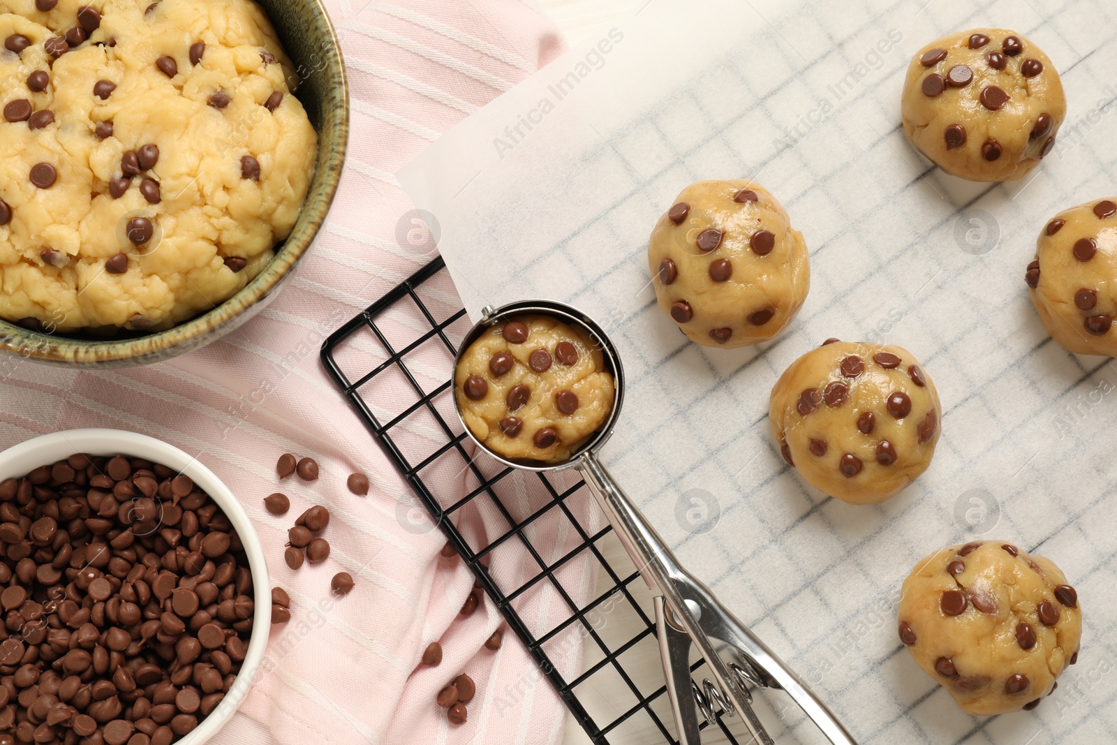 Photo of Bowl with dough and uncooked chocolate chip cookies on table, flat lay