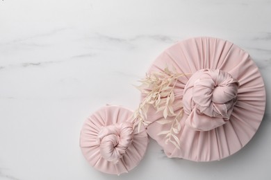 Photo of Furoshiki technique. Gifts packed in pink fabric and dried branches on white marble table, flat lay. Space for text