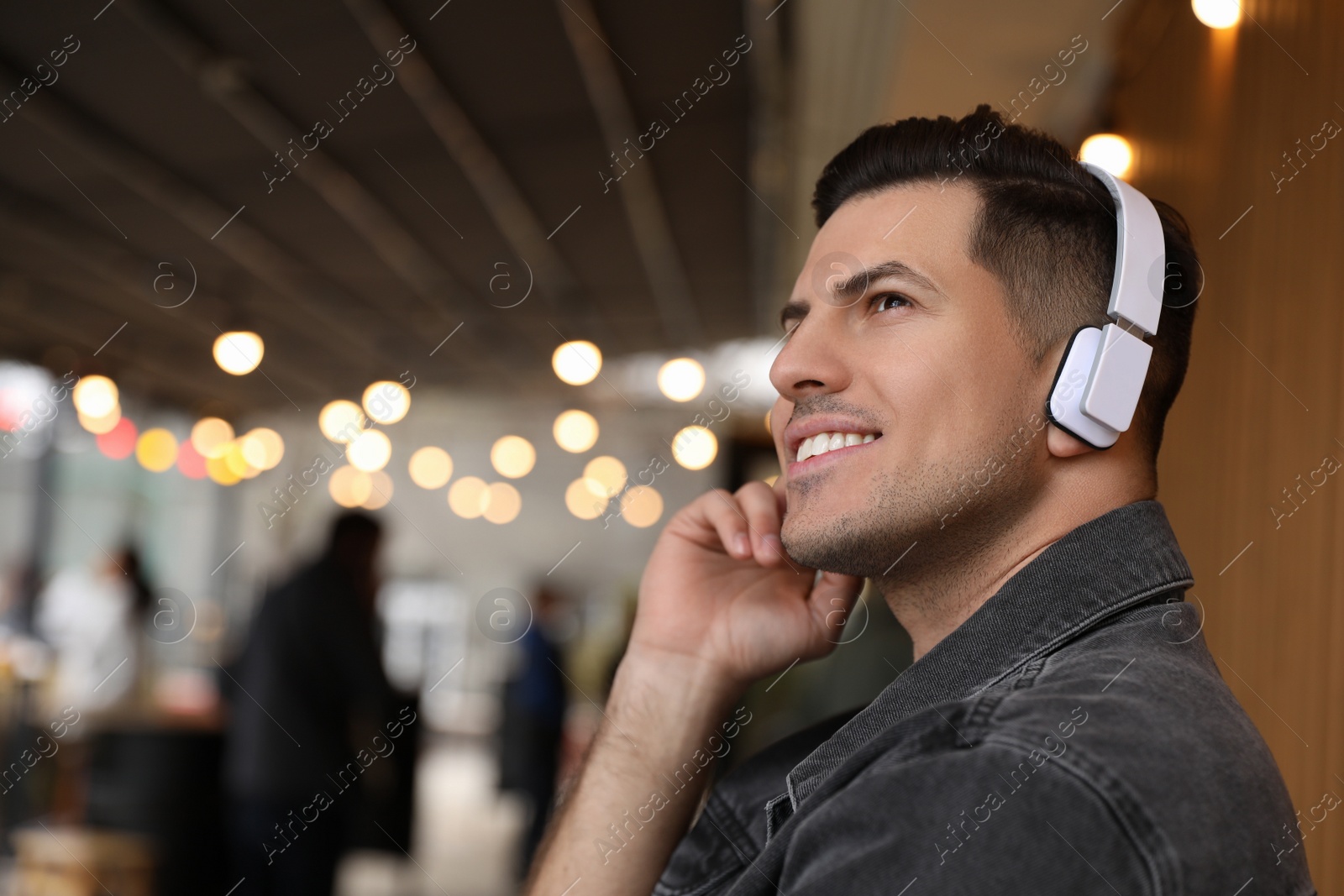 Photo of Handsome man with headphones listening to music in outdoor cafe, space for text