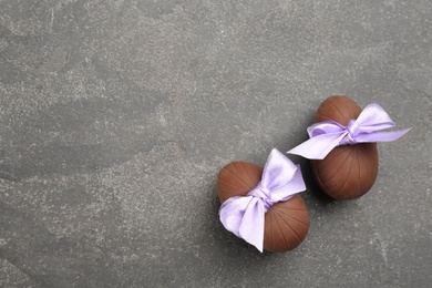 Photo of Sweet chocolate eggs with violet bows on grey table, flat lay. Space for text