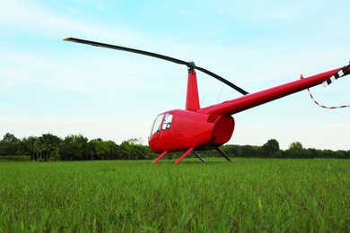 Photo of Modern red helicopter on green grass outdoors, low angle view