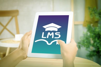 Image of Learning management system. Woman using tablet at table, closeup. Open book and graduate cap icons with abbreviation LMS on screen