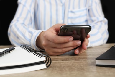 Woman with smartphone at wooden table in office, closeup