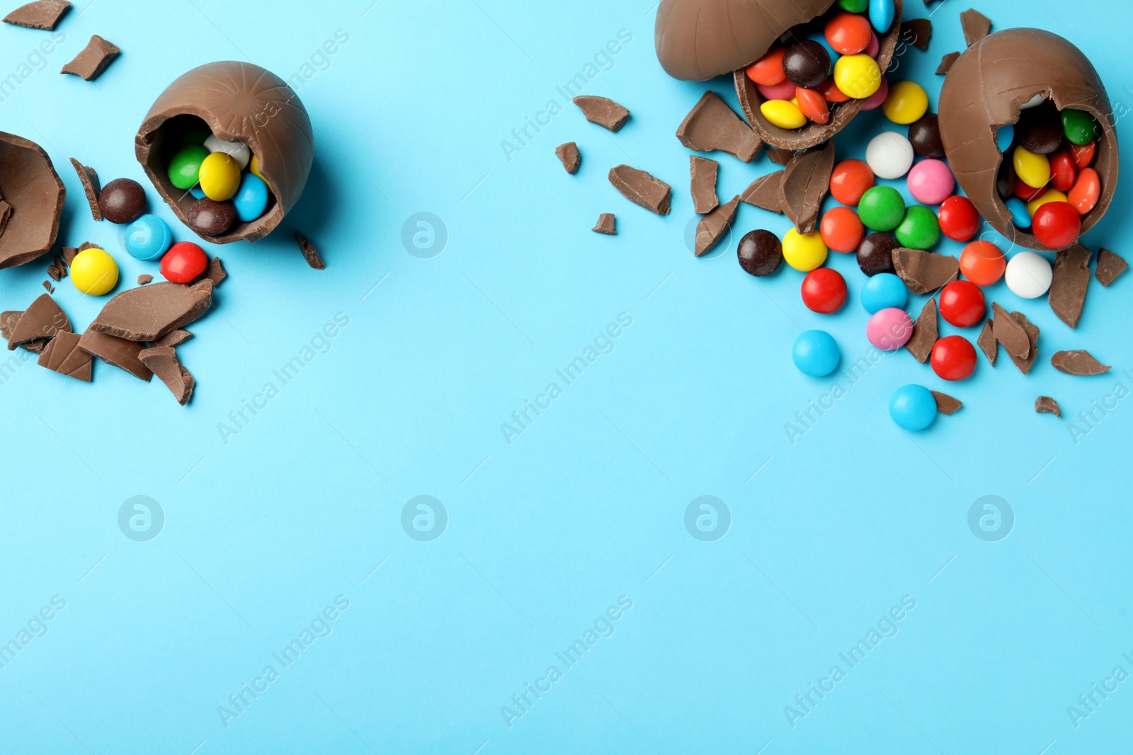 Photo of Broken chocolate eggs with candies on light blue background, flat lay. Space for text