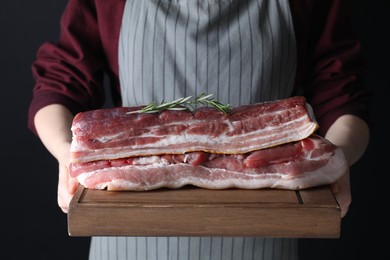 Photo of Woman holding wooden board with pieces of raw pork belly on black background, closeup