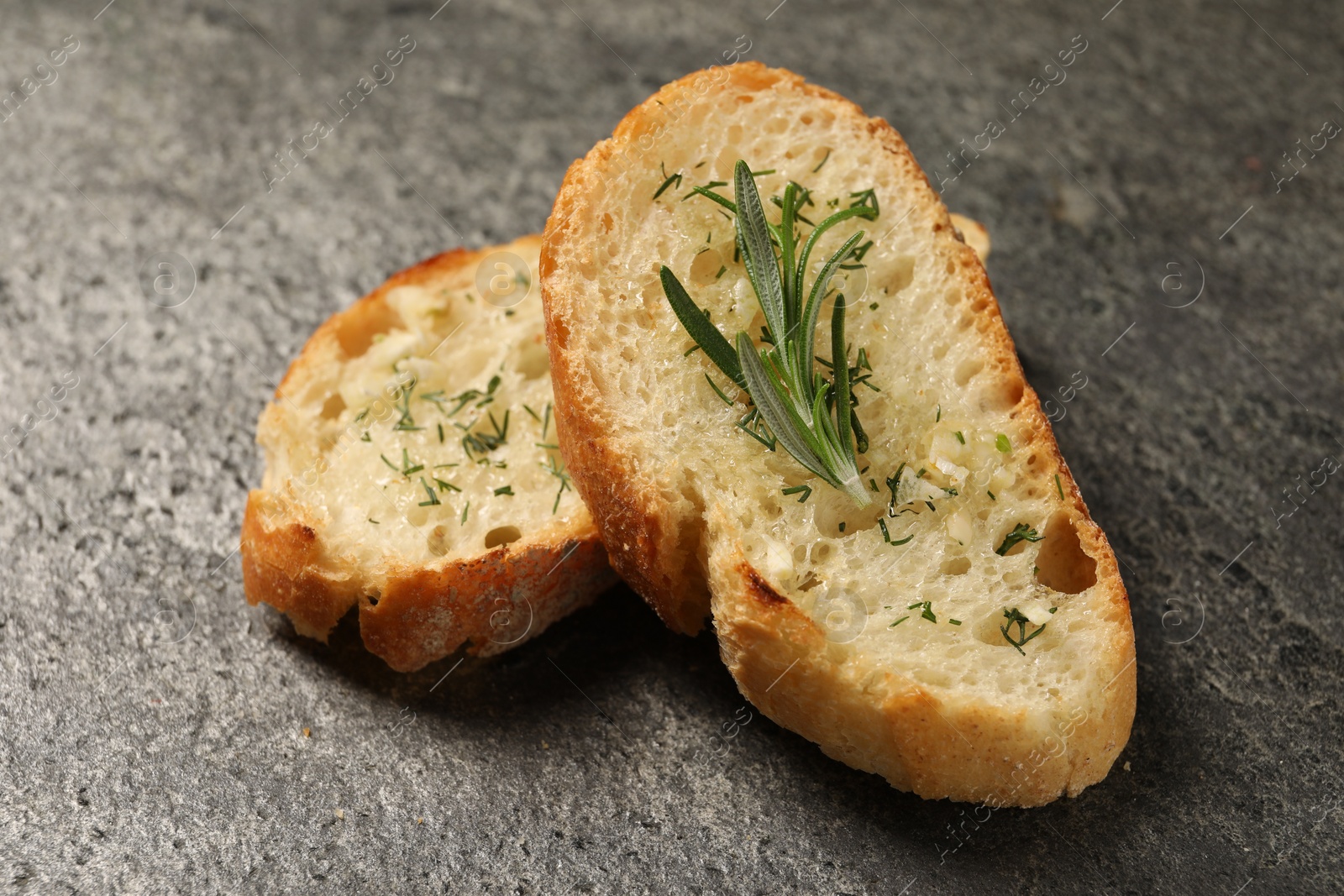 Photo of Tasty baguette with garlic, rosemary and dill on grey textured table, closeup