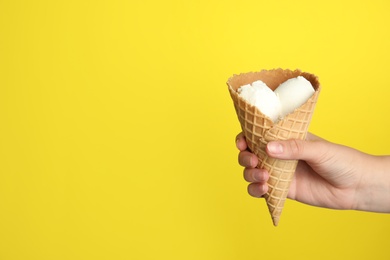 Photo of Woman holding delicious ice cream in wafer cone on yellow background, closeup. Space for text