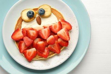 Photo of Creative serving for kids. Plate with cute owl made of pancakes, strawberries, cream, banana and almond on white wooden table, top view