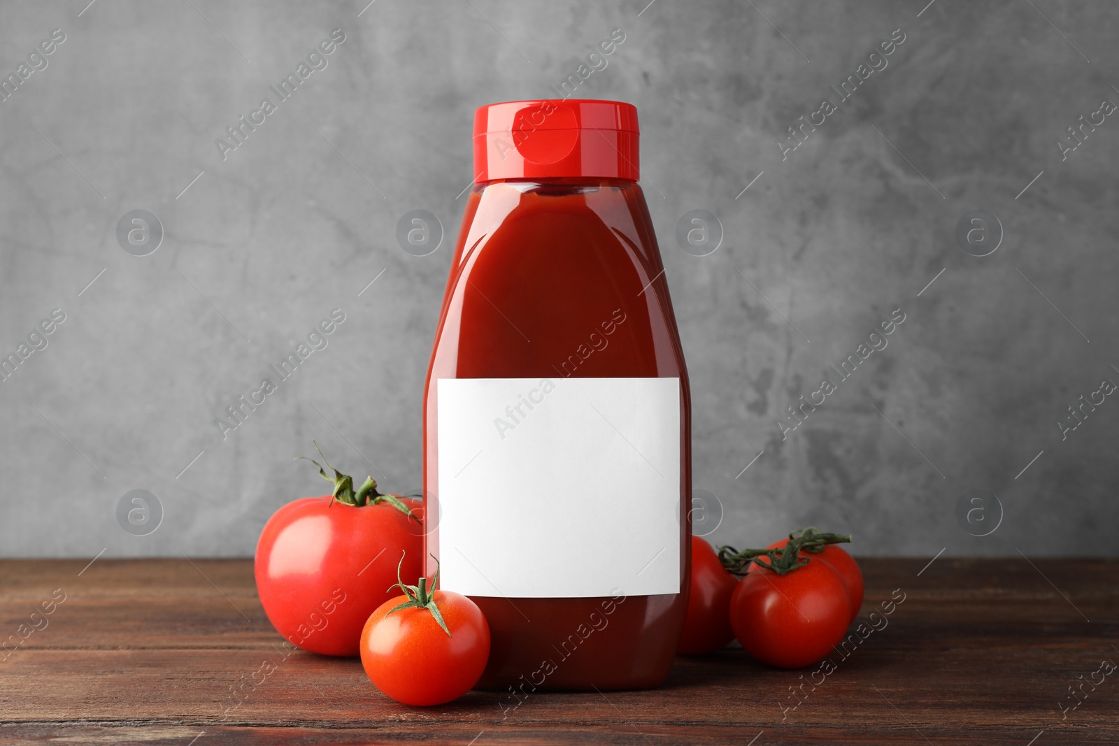 Photo of Bottle of tasty ketchup and tomatoes on wooden table. Space for text