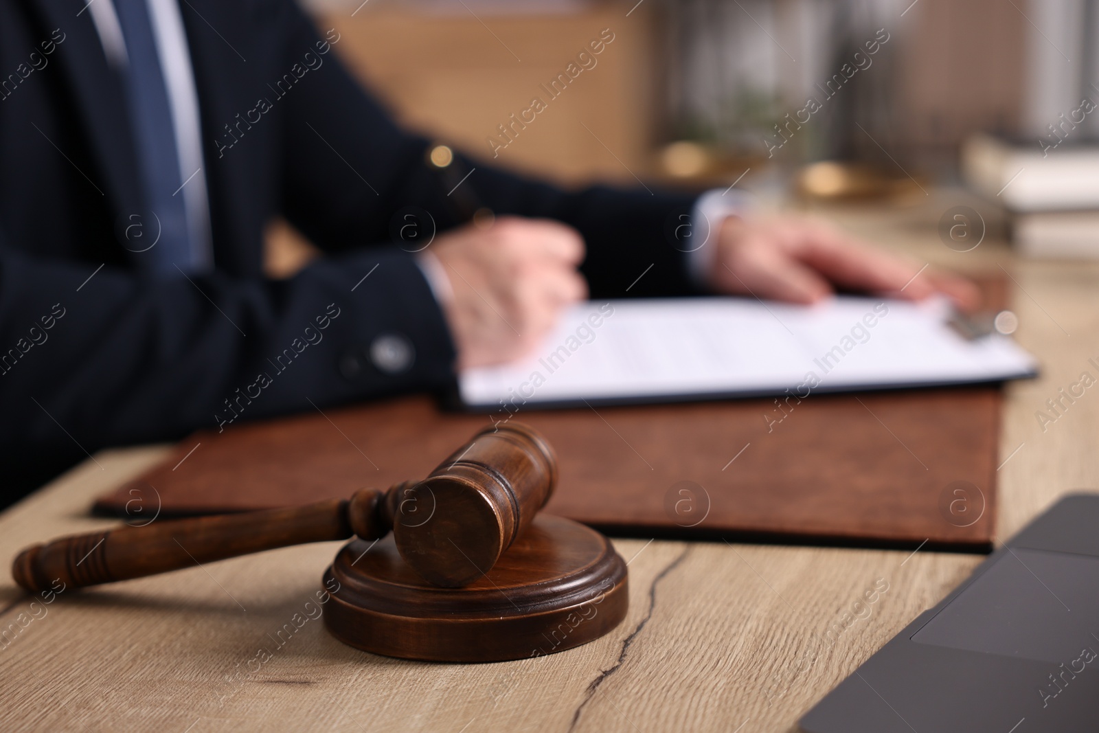 Photo of Notary writing notes at wooden table in office. focus on gavel