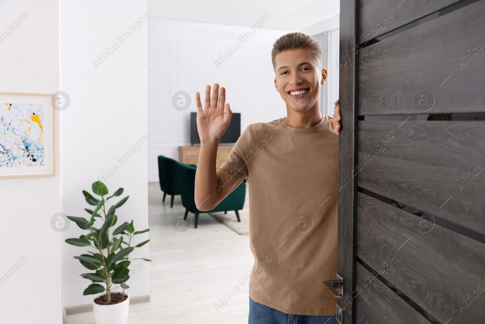 Photo of Happy man waving near door, space for text. Invitation to come indoors