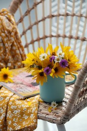 Beautiful bright flowers in light blue cup near magazine and fabric on rattan armchair