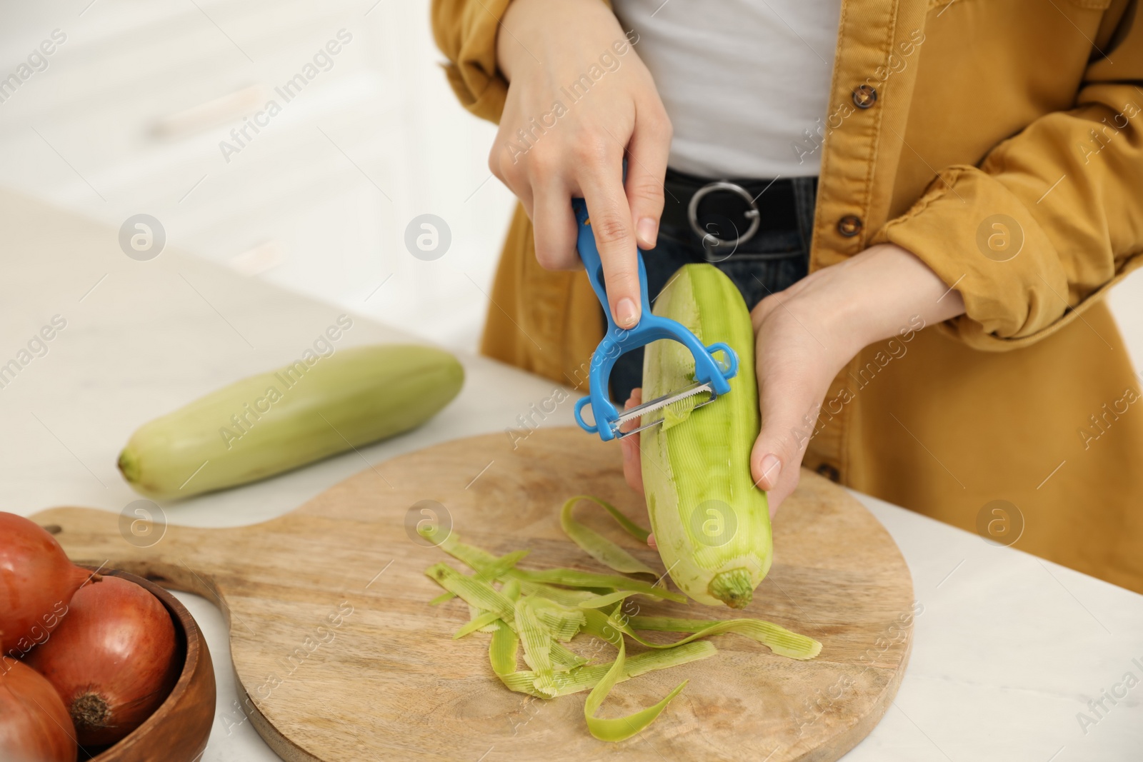 Photo of Woman peeling zucchini at kitchen counter, closeup. Preparing vegetable