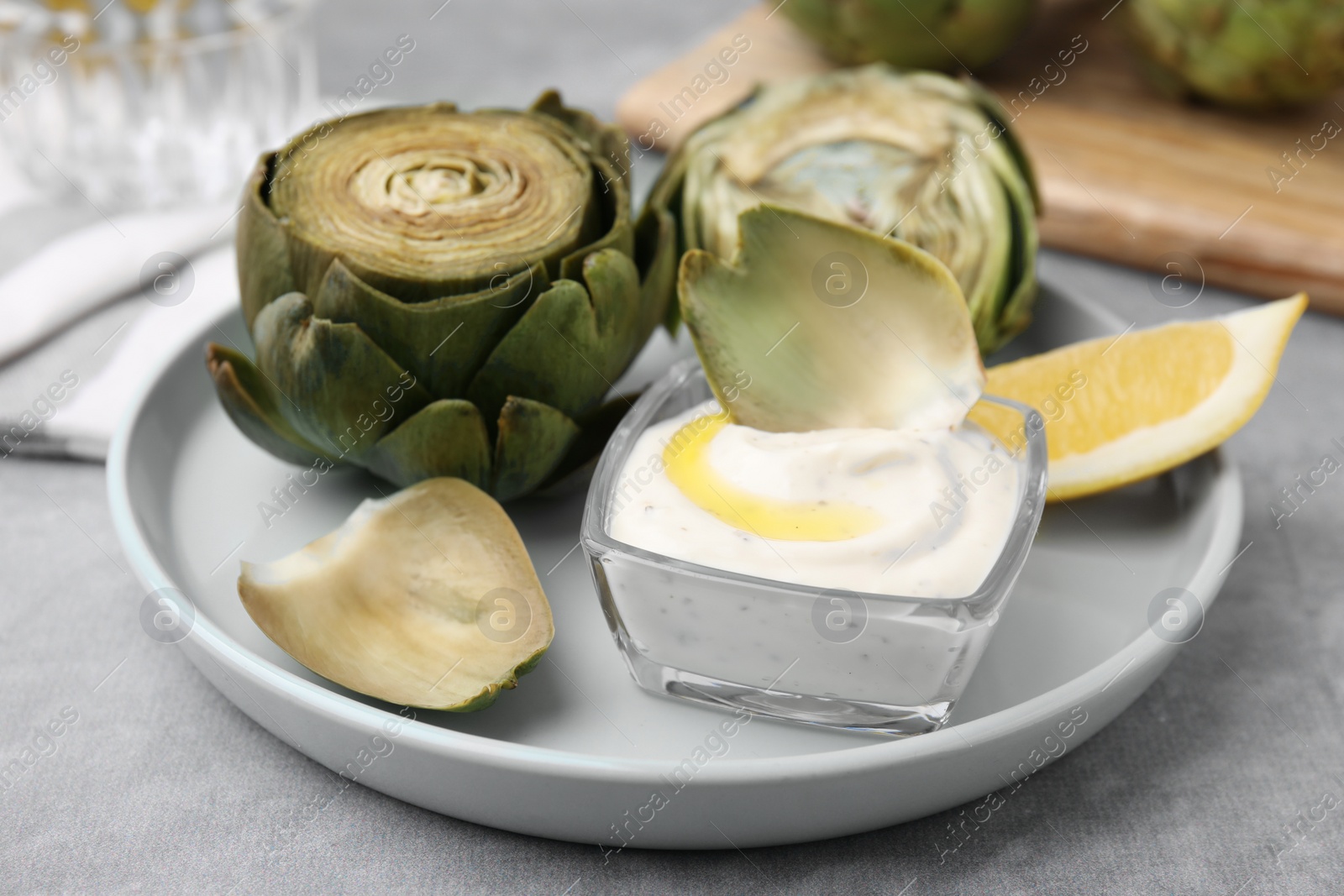 Photo of Delicious cooked artichokes with tasty sauce served on grey table, closeup