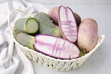 Purple and green daikon radishes in wicker basket on light grey table