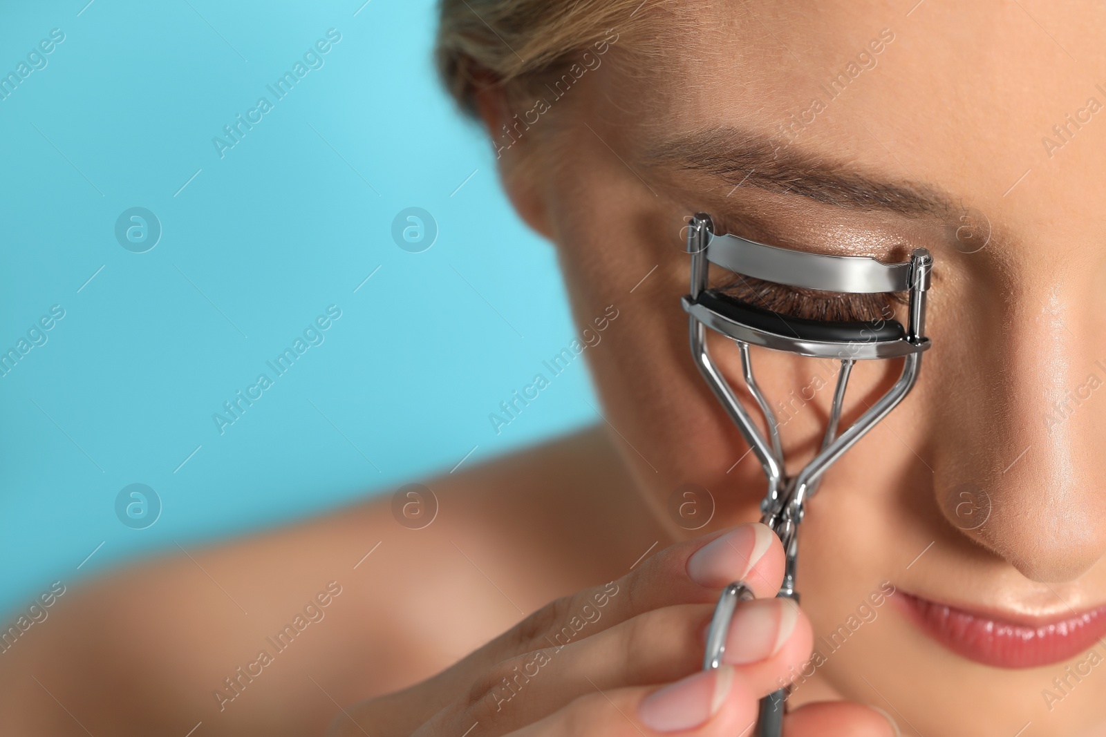 Photo of Young woman using eyelash curler on light blue background, closeup