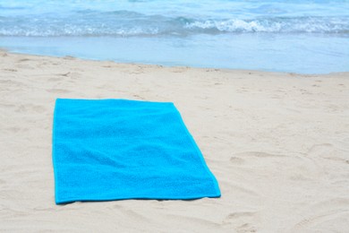 Blue towel on sandy beach near sea, space for text