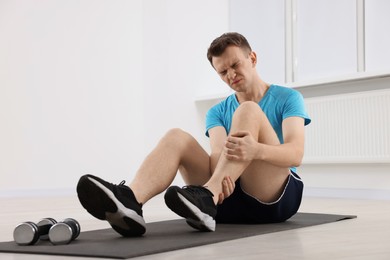 Man suffering from leg pain on mat indoors