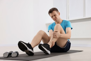 Photo of Man suffering from leg pain on mat indoors