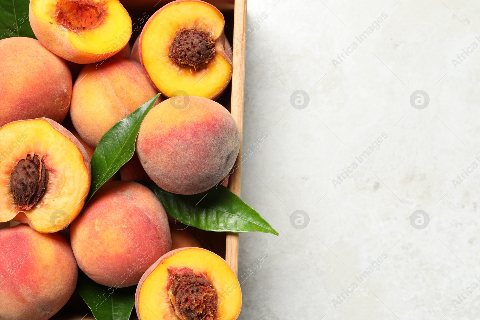 Photo of Delicious juicy peaches and leaves in crate on light grey textured table, top view. Space for text