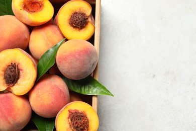 Photo of Delicious juicy peaches and leaves in crate on light grey textured table, top view. Space for text