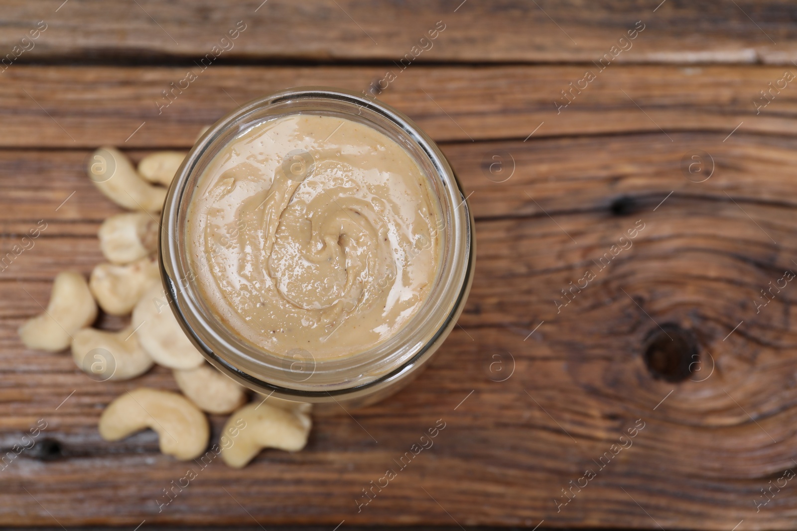 Photo of Tasty cashew nut paste in jar on wooden table, top view. Space for text