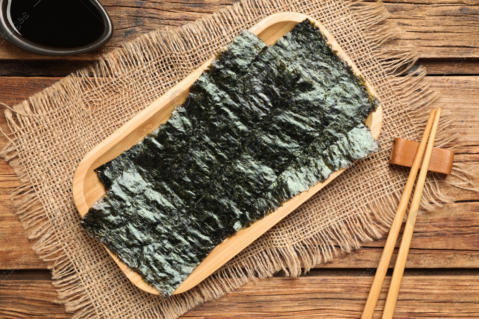 Photo of Dry nori sheets, soy sauce and chopsticks on wooden table, flat lay