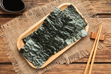 Dry nori sheets, soy sauce and chopsticks on wooden table, flat lay