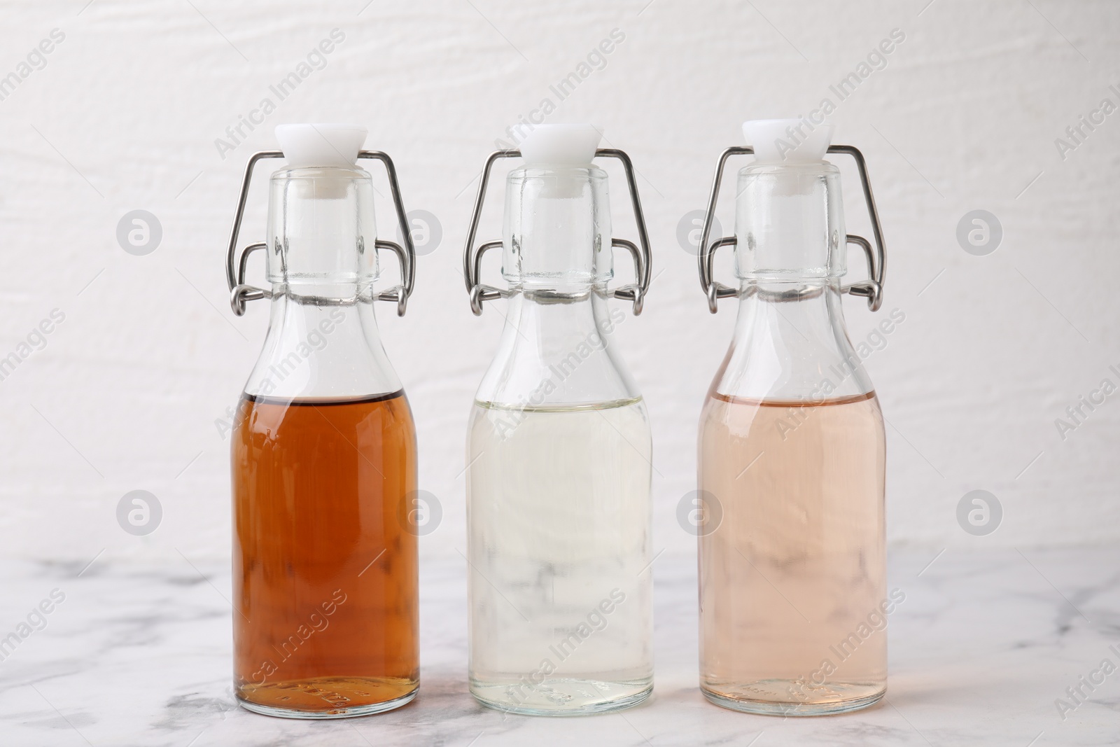 Photo of Different types of vinegar in bottles on light marble table, closeup