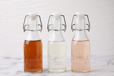 Different types of vinegar in bottles on light marble table, closeup